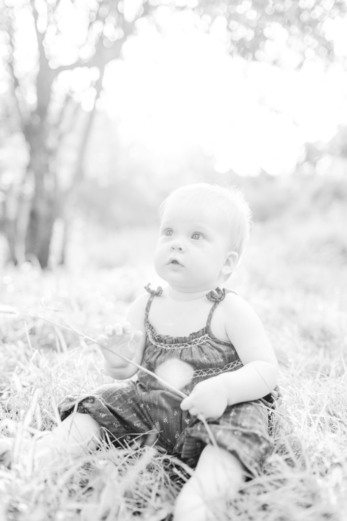 Metrowest Boston Family Photographer - Black and white photo of young baby in the outdoors, in a field at sunset.  Family photos in Sherborn, Massachusetts with Corinne Isabelle Photography