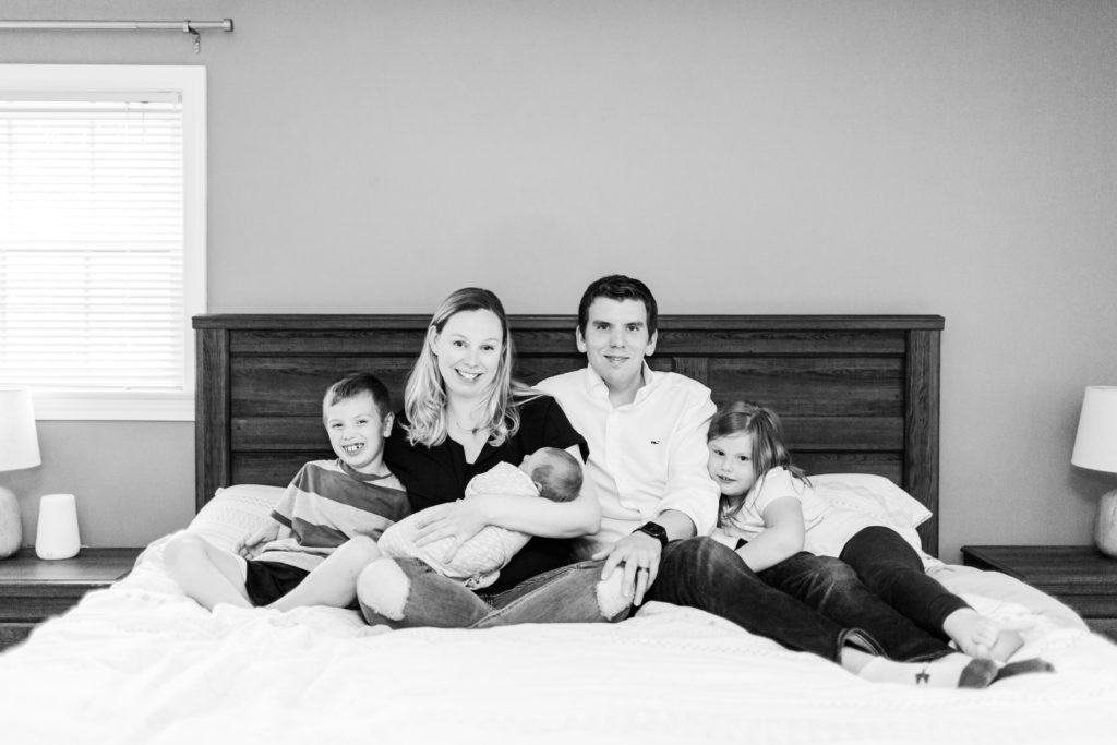 Boston Newborn Photographer - Family sitting on bed with newborn baby wrapped up in Holliston, Massachusets