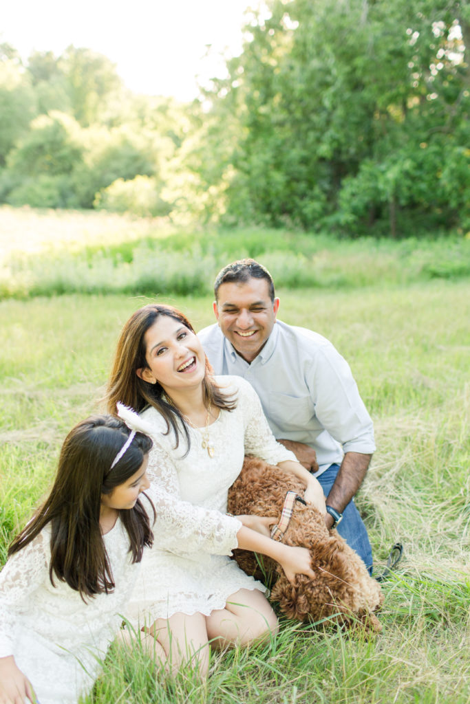 Holliston Family Photographer - Young family sitting in field with their fluffy dog, smiling for family photo session in Sherborn Massachusetts.
