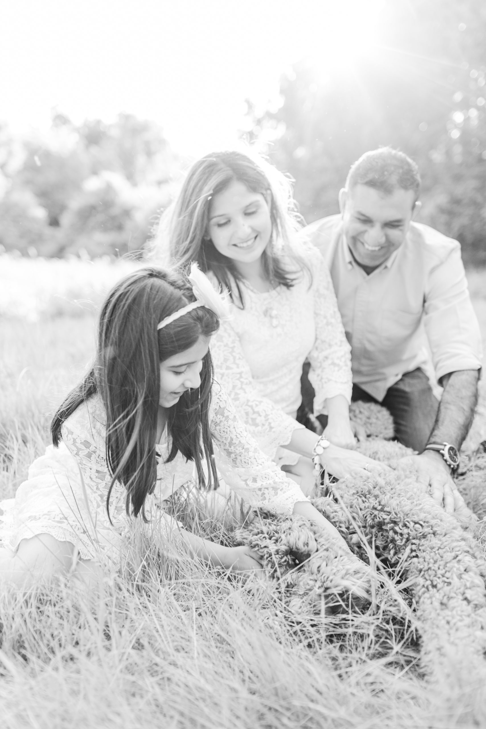 Young family sitting in field with their fluffy dog, smiling for family photo session in Sherborn Massachusetts.