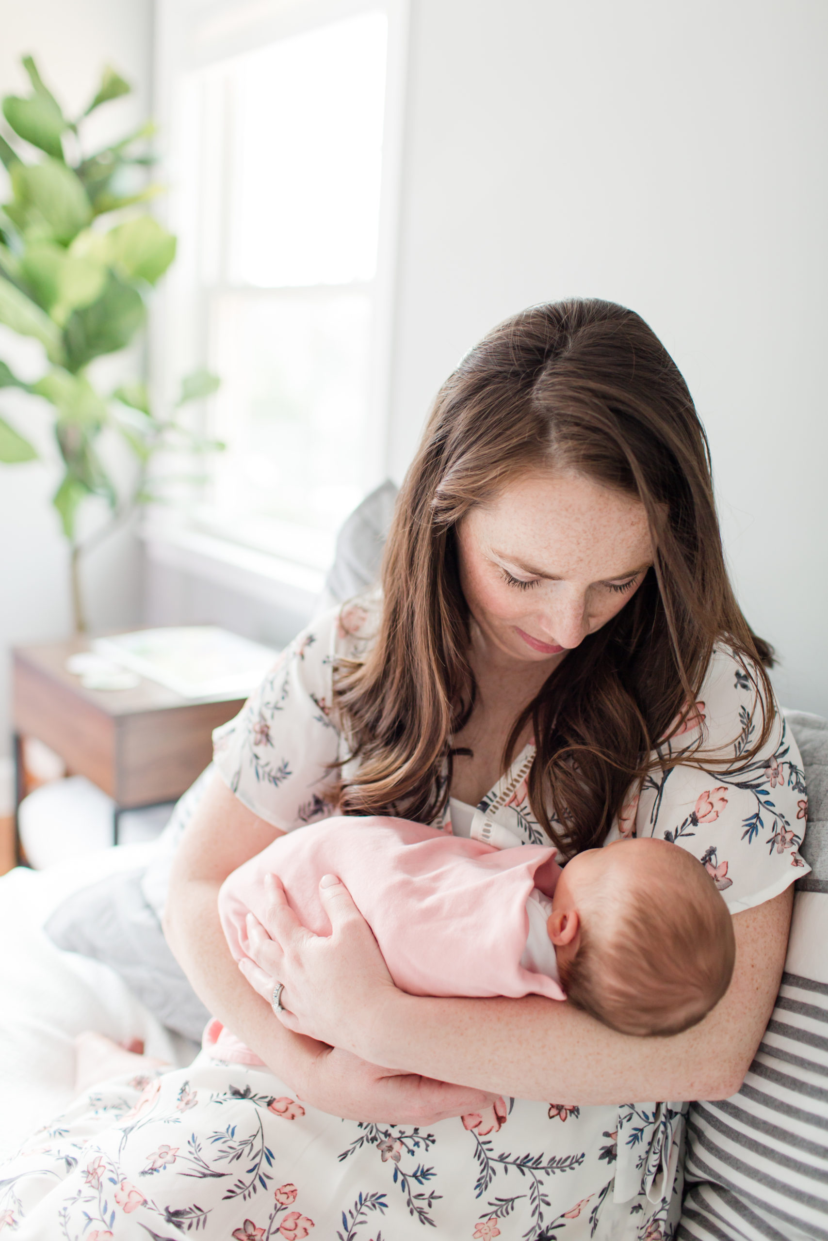 Young mom holding her baby in natural light bedroom for photo session.