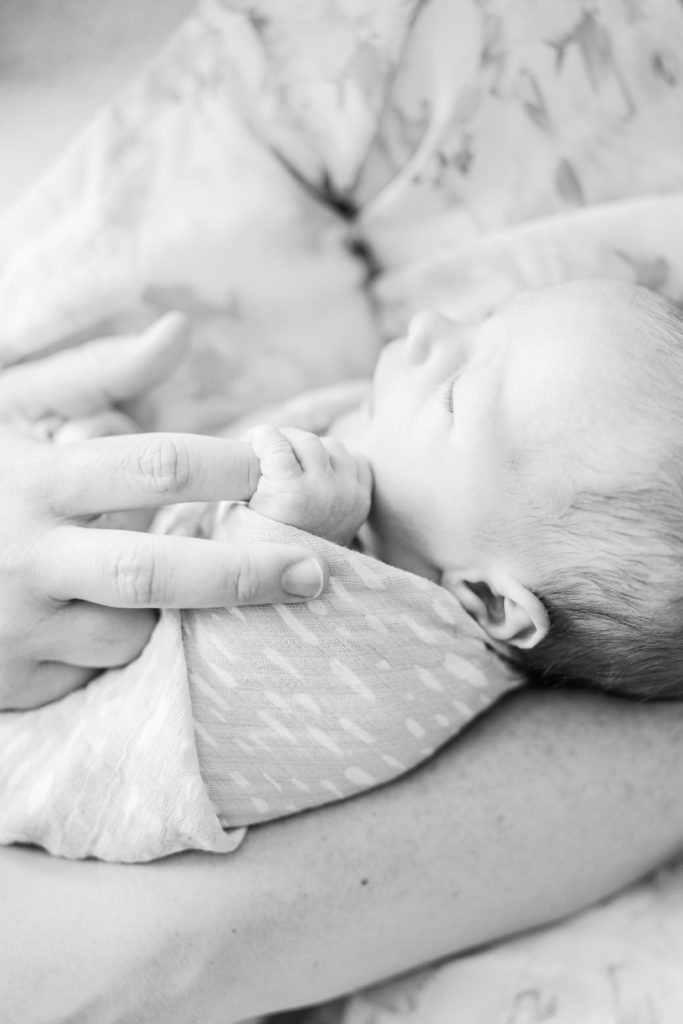 Newborn baby being held by their mother and grasping her hand during photo session with Holliston Newborn Photographer Corinne Isabelle