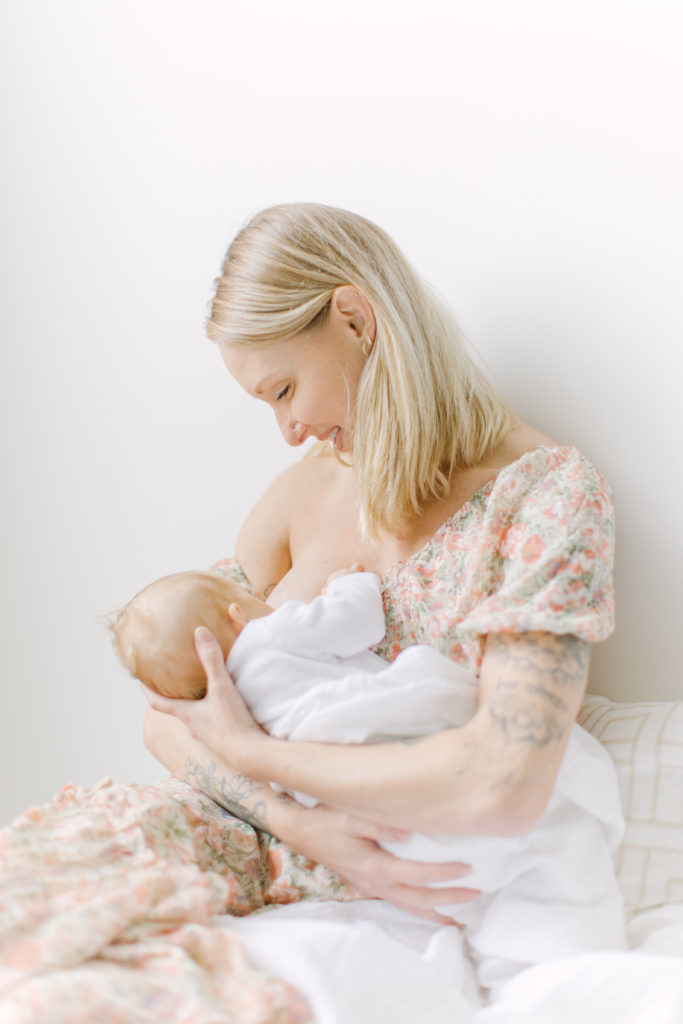 Young mom holding and breastfeeding her newborn baby during photos with Boston baby photographer Corinne Isabelle