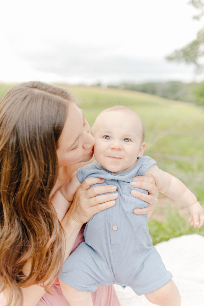 Mom kissing baby boy outdoors during a lifestyle family session with Boston Family Photographer Corinne Isabelle