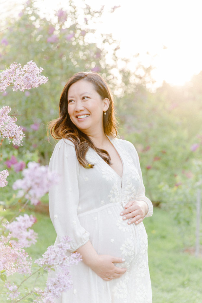Expecting mom posing for maternity photos with Boston Maternity Photographer Corinne Isabelle Photography at the Arnold Arboretum with lilac blooms
