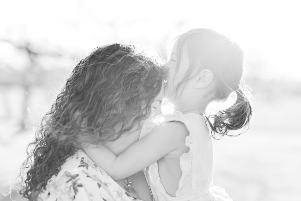 Mom holding being kissed by young daughter during outdoor spring photo shoot with Boston Motherhood Photographer Corinne Isabelle Photography