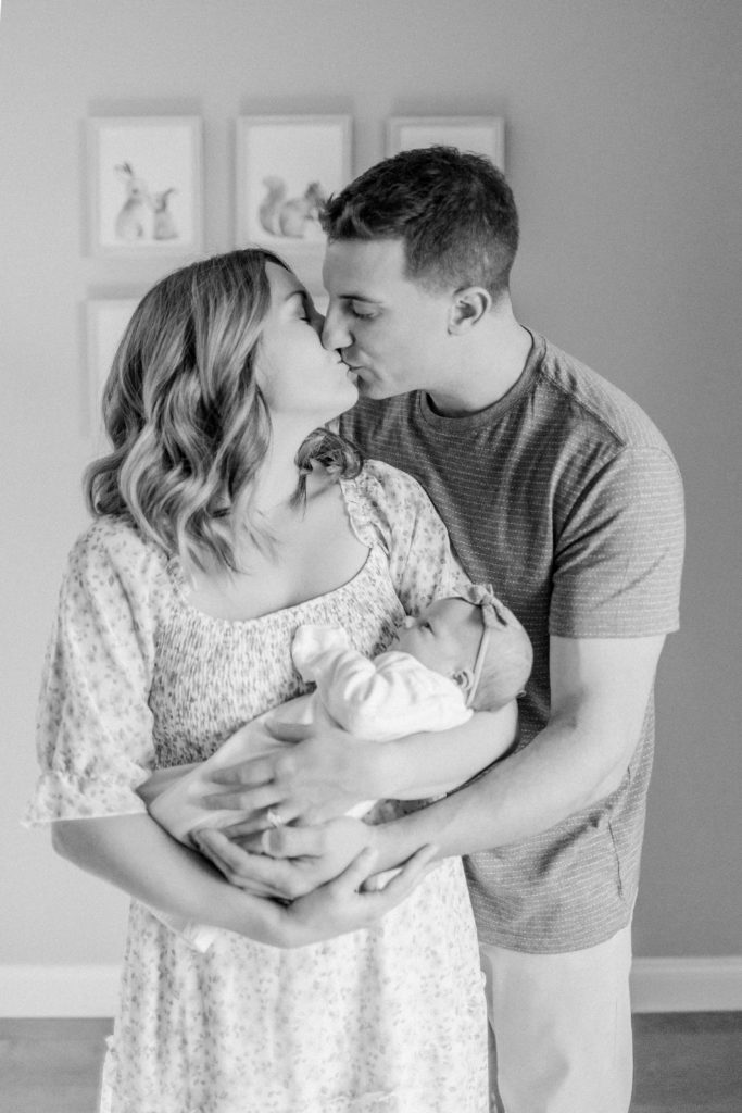 Young mom and dad embracing and holding their newborn baby during in-home photo session with Medway Newborn Photographer Corinne Isabelle