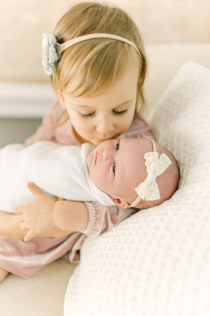 Toddler girl holding her new baby sister during photo session with Medway Newborn Photographer Corinne Isabelle