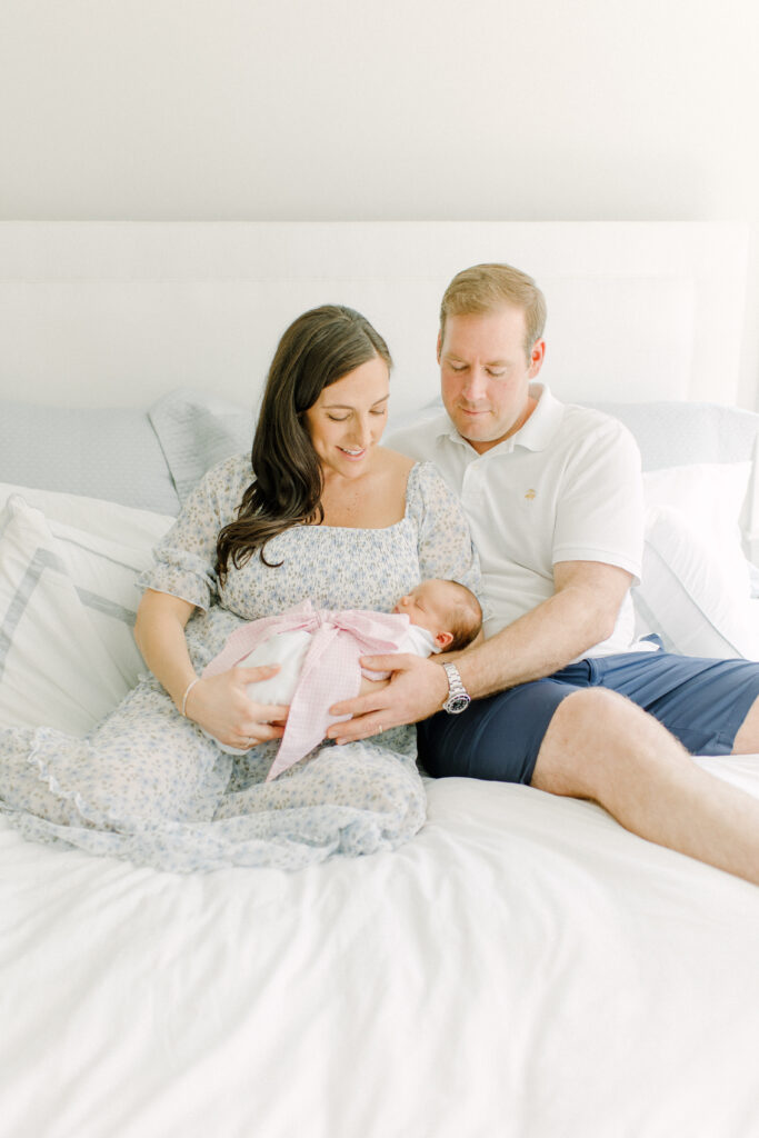 Newborn baby girl sleeping while her mom and dad hold her on their bed during in-home photo session with Boston area newborn photographer Corinne Isabelle