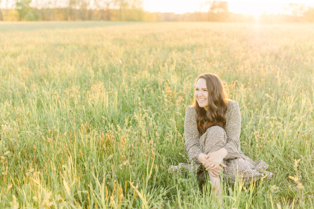 Corinne Isabelle, a Boston area family photographer sitting in a field during golden hour.