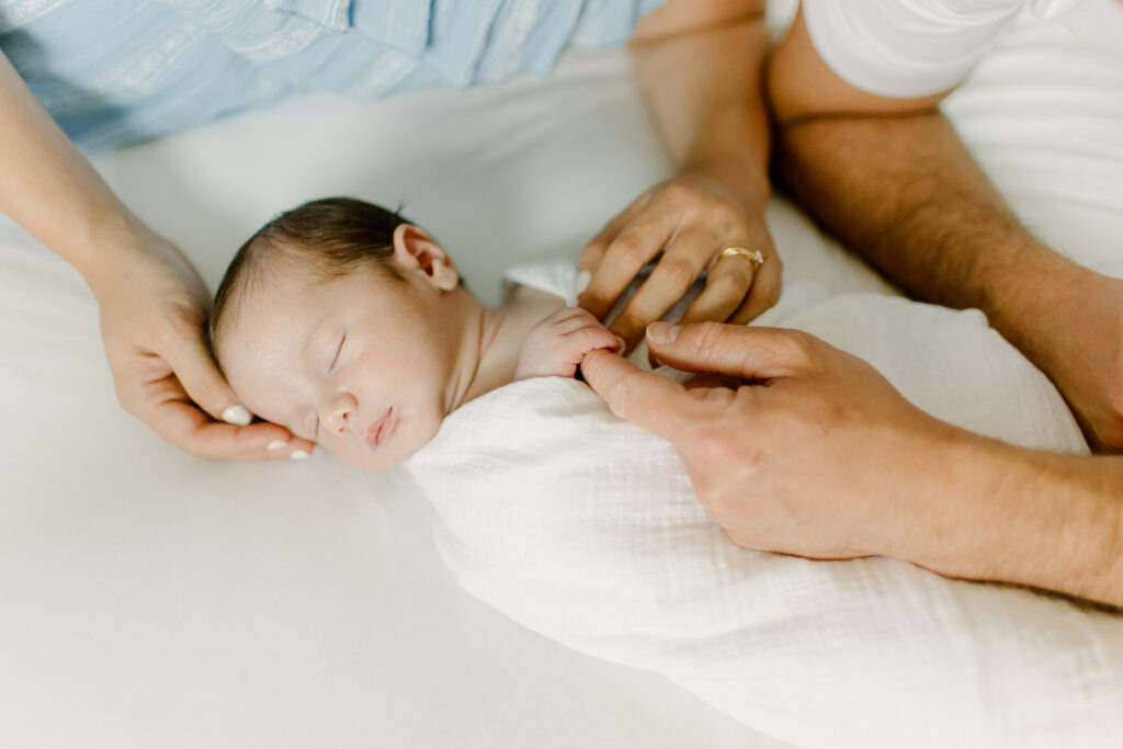Newborn baby boy sleeping while grasping his dad's finger during newborn photo session with Boston newborn photographer Corinne Isabelle