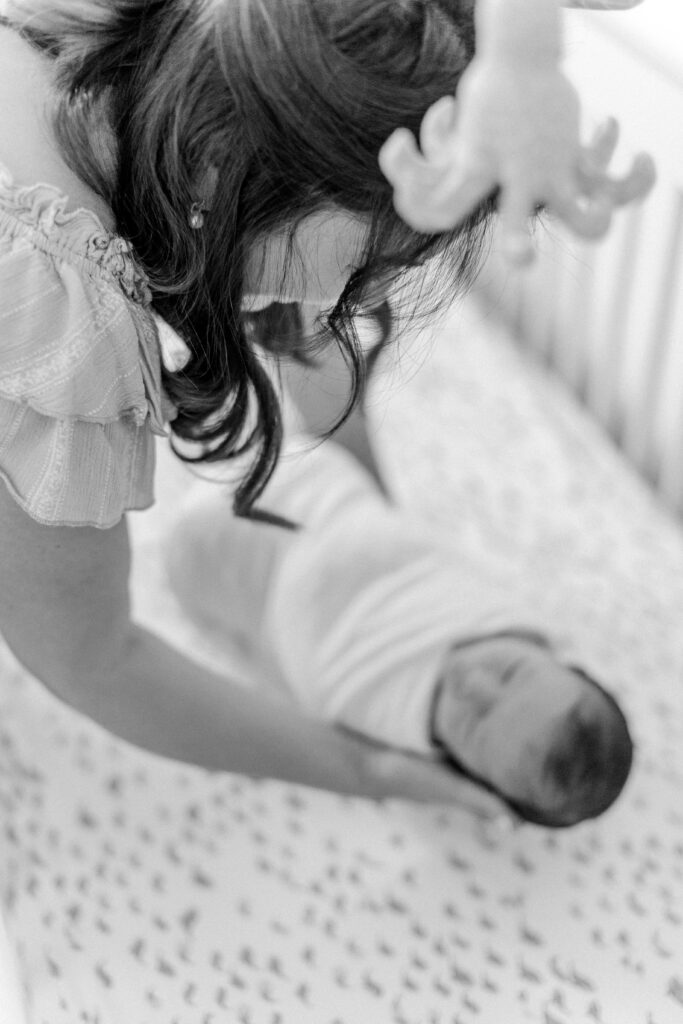 New mom laying down her baby in his crib during photo session with Boston newborn photographer Corinne Isabelle